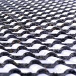 Close-up view of a textured roof with overlapping, curved black and white ceramic tiles, showing signs of weathering and dirt accumulation.